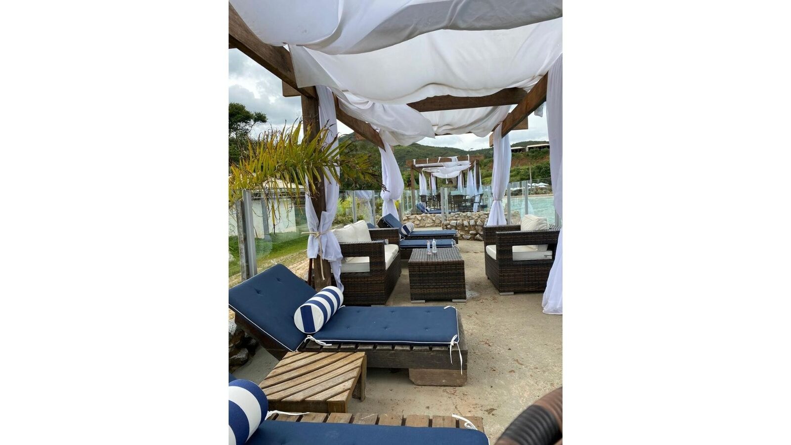 Cabana com cortinas e sofás de vime à beira da piscina